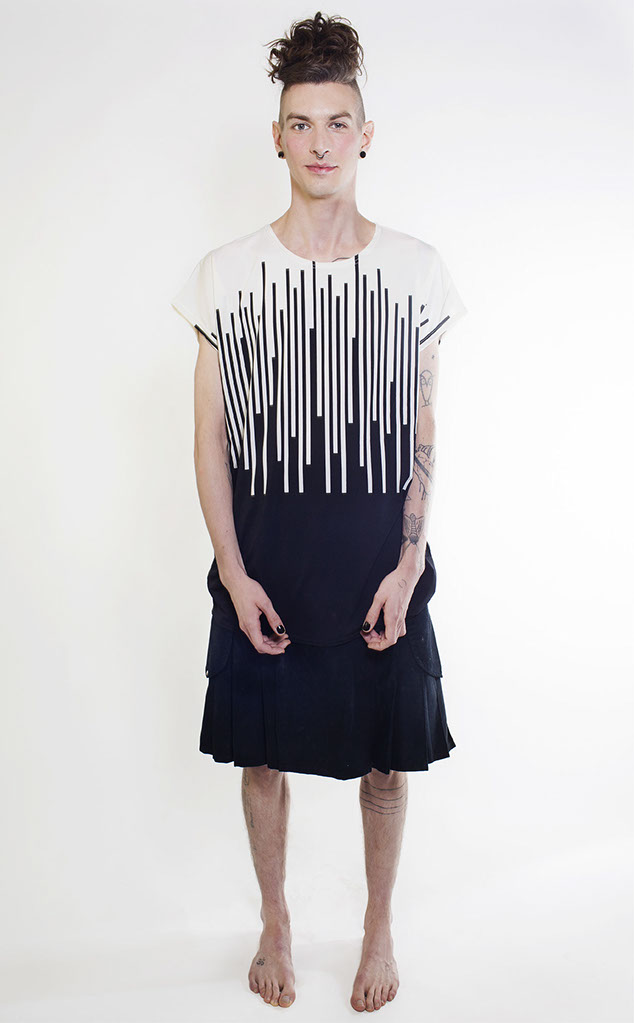 colour photograph of a man in a black kilt and a black and white vertically striped top.. The sided of his head are shaven, The long hair on the top of his head is worn in a beehive style. He has half open fists. His lips and cheeks have an orange hue.